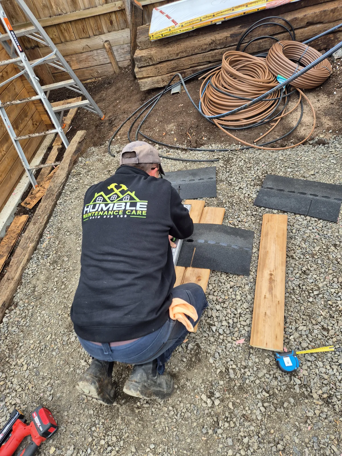 Drew in his Humble Maintenance Care hoodie laying roof shingles on-site