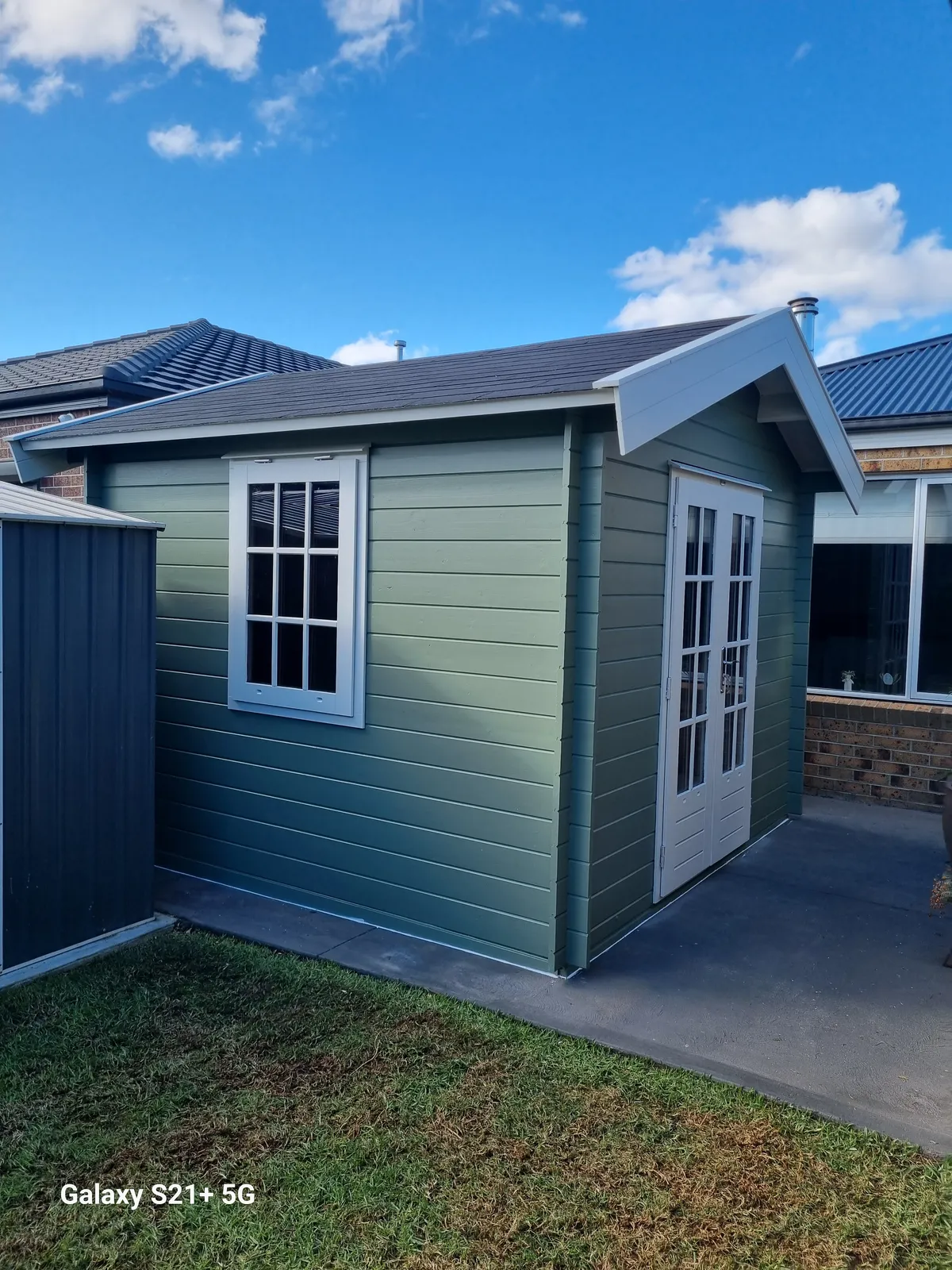 Side view of the finished sage-green cabin with white-framed window
