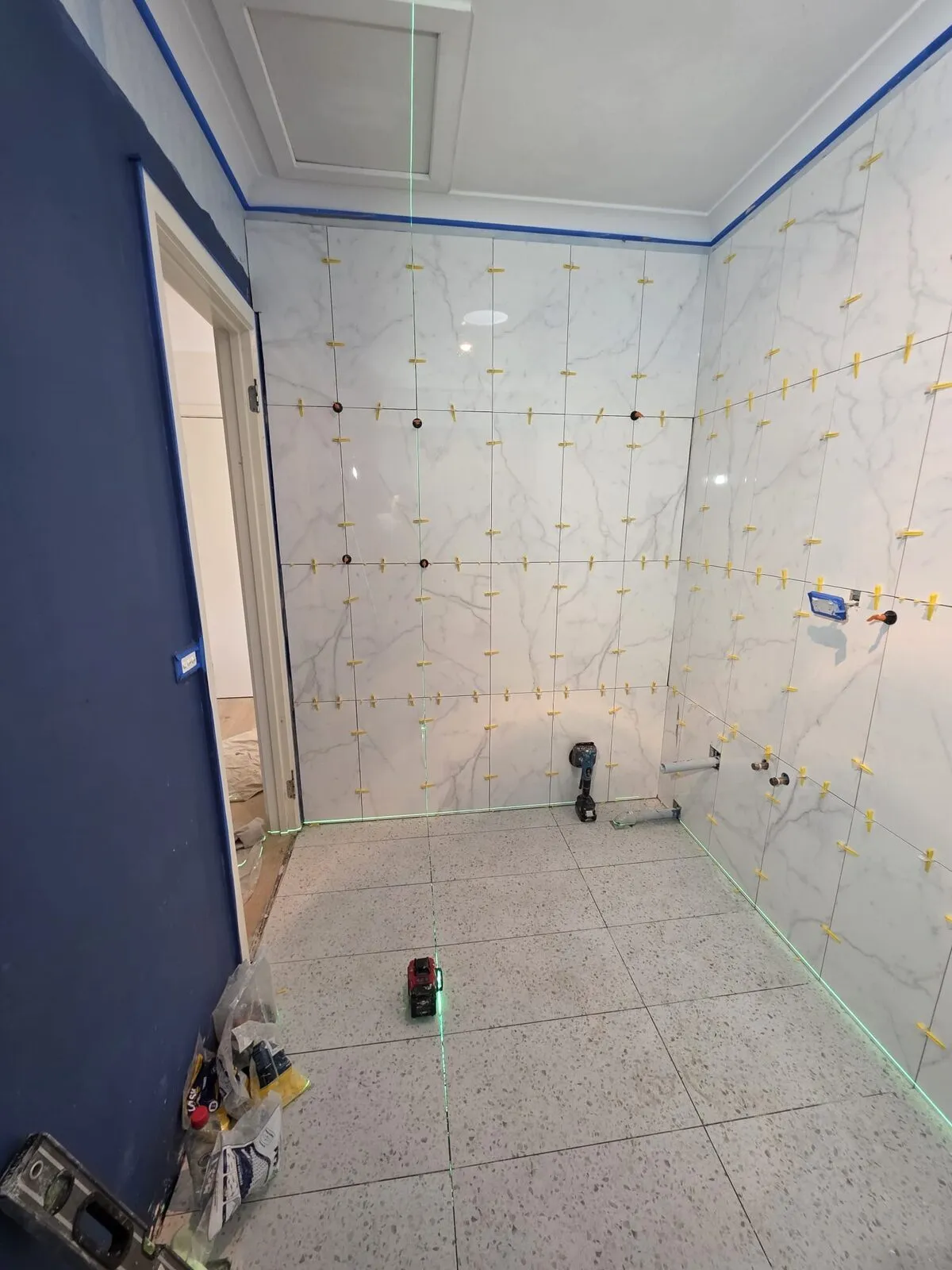 Marble-look wall tiles being set with levelling clips and laser line guides
