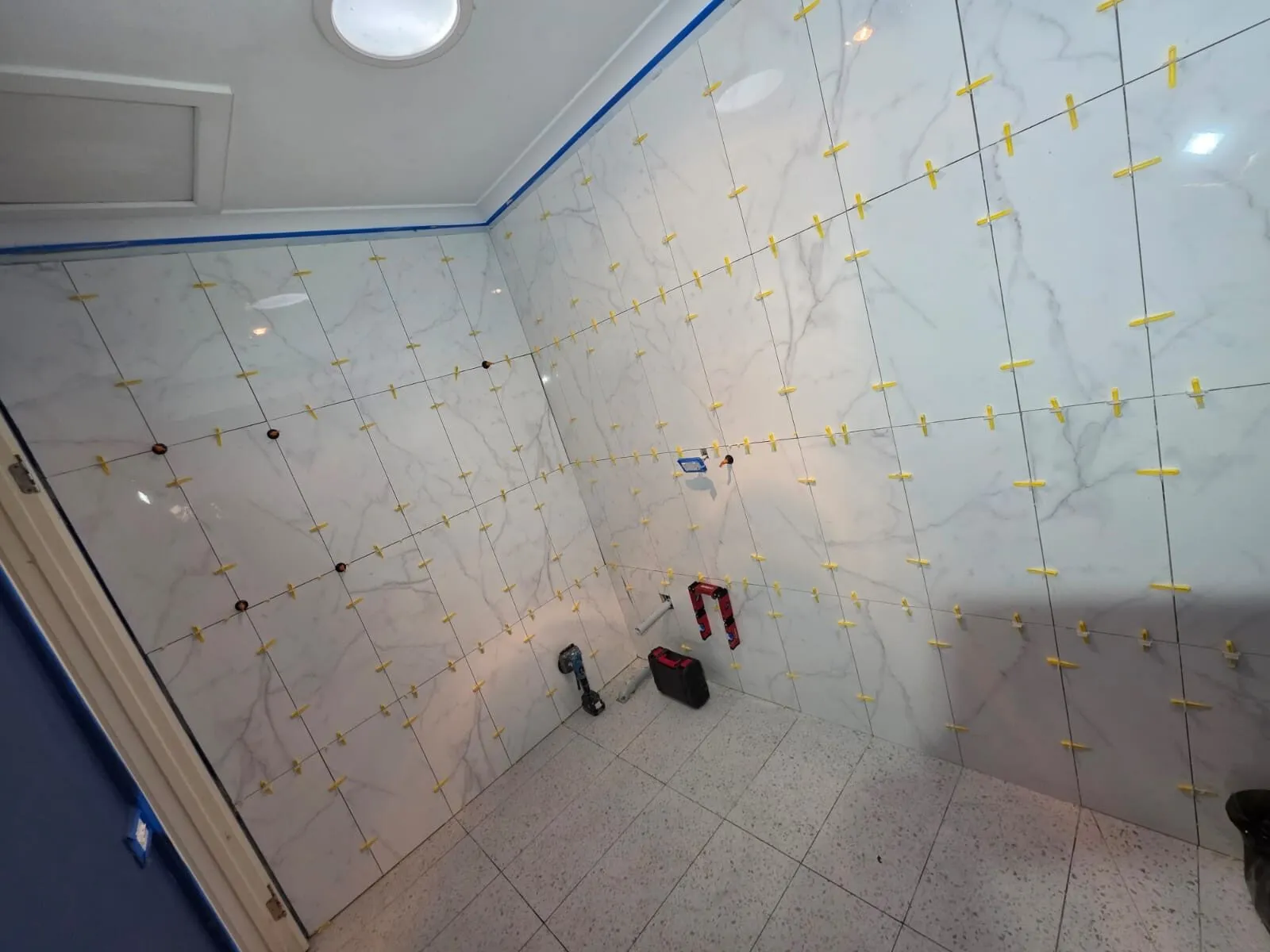 Large-format wall tiles in progress with levelling spacers across both walls